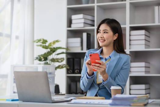 Young female accountant in a modern office, smiling and using a smartphone, surrounded by office supplies and documents, showcasing professionalism and efficiency.