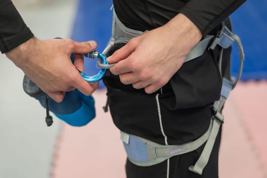 A Caucasian man puts on a climbing harness before training on a climbing wall. Climber fastens his carabiner