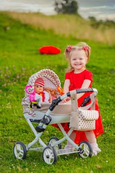 little girl plays with a doll and a stroller on the lawn