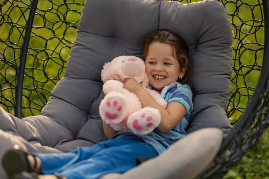 child hugging a teddy bear while sitting in a hanging chair