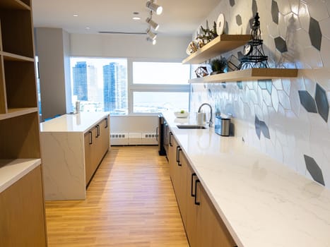 A compact bar area within a hotel's fitness center, featuring a striking geometric backsplash and floating wooden shelves, with a panoramic window offering views of the urban skyline.