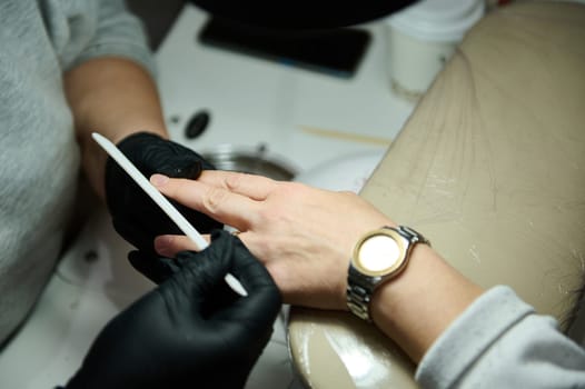 A beautician files a woman's nails during a manicure session in a beauty salon. Professional nail care and personal grooming.