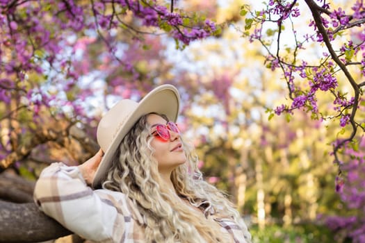 Beautiful woman in hat near blossoming tree on spring day, space for text.
