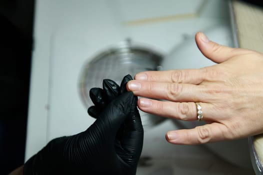 Close-up of a beautician wearing black gloves providing a manicure service to a customer in a beauty salon.