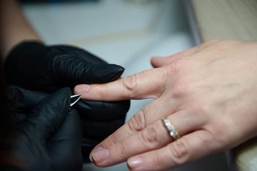 Close-up of a manicure process in a beauty salon. Gloved hands providing nail care services to a client.