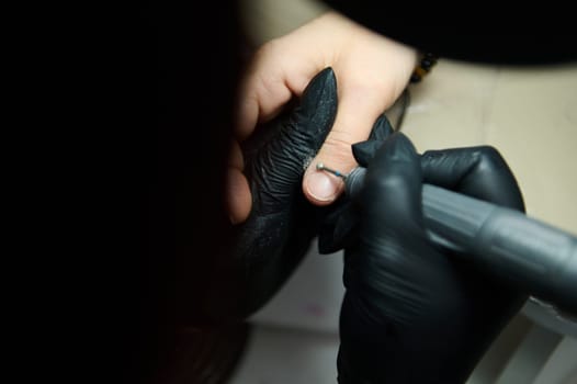 Close-up of professional beauty salon work, showing detailed nail treatment with a drill and black gloves.