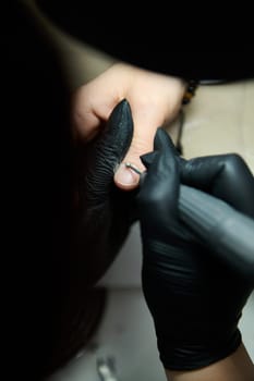 A detailed close-up capturing a beauty salon manicure procedure with gloved hands using a tool for nail care.