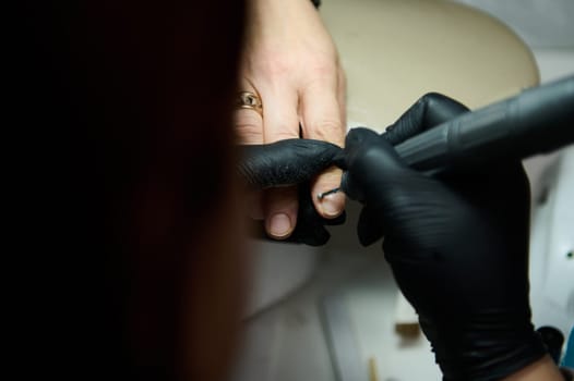 Close-up of a professional manicure being performed at a beauty salon. Person receiving nail treatment by technician wearing black gloves.