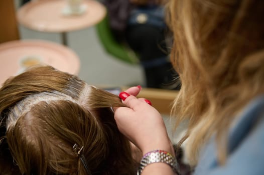 Hairdresser applying hair dye to client at beauty salon. Close-up view of professional hair treatment process.