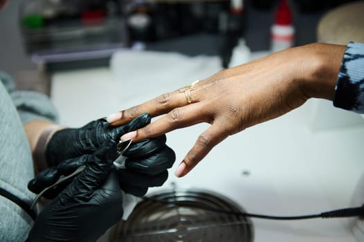 A nail technician wearing gloves carefully applies a manicure to a client's hand in a beauty salon, showcasing luxury nail care services.