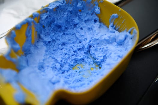 Close-up image of blue hair dye mixture in a yellow container at a beauty salon, ready for hair coloring.