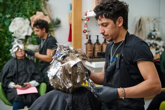 Hairdresser carefully applying color to customer's hair using foil technique in a beauty salon. Detailed view showing professional service and client relaxation.