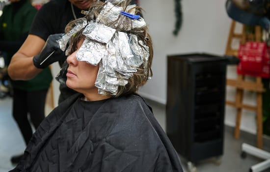 A woman receiving a hair coloring treatment with aluminium foils at a beauty salon. Professional hairstylist applying dye.