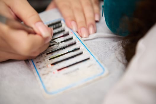 Close-up of a beauty professional applying eyelash extensions at a salon. Detailed view of tools and lashes.