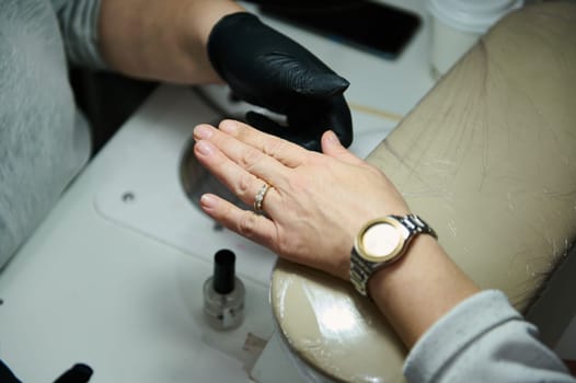 A hand is being treated in a beauty salon. The image shows a professional manicurist working on a client's nails with care and attention to detail.