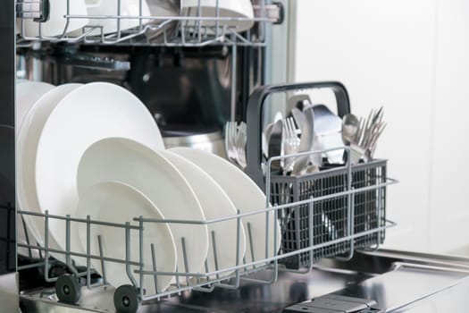 Opened dishwasher machine with clean tableware, white porcelain plates. Convenient modern technologies in the kitchen