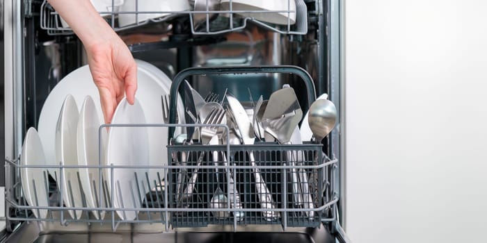 Female hand unloading dishwasher with tableware. Kitchen appliances, lifestyle view. Woman takes a plate from the dishwasher. Concept of modern technologies in the kitchen