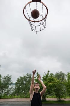 A Caucasian man shoots a ball into a basketball basket outdoors. Vertical photo