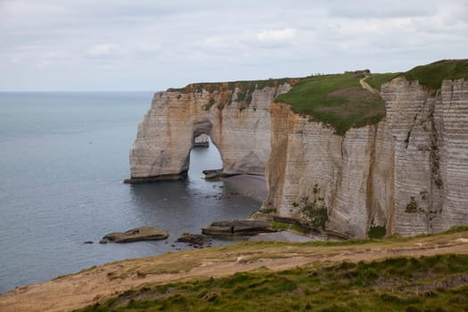 Landscape photo of tall, steep limestone cliffs by the ocean with one with a hole in it creating an arch