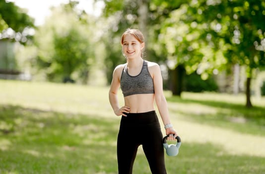 Teenage Girl Exercises With Kettlebell In Park During Summer