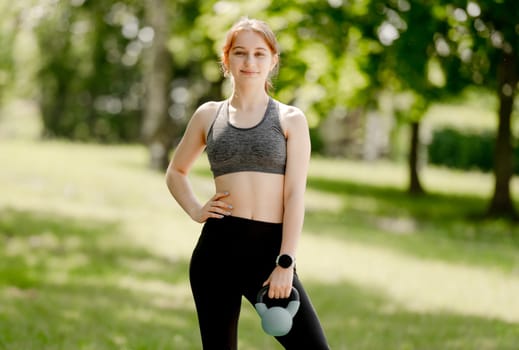 Teenage Girl Exercises With Kettlebell In Park During Summer