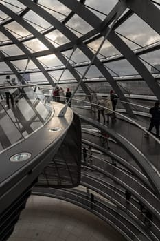 Berlin, Germany - Dec 20, 2023 - Several tourists walking at ramps inside the futuristic glass dome. A curved walkway stretches in spirals upwards on top inside the Reichstag building. Contemporary architecture of the Cupola of the Reichstag dome, a major tourist attraction of the berlin city, Space for text, Selective focus.