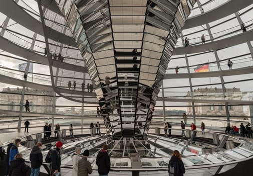 Berlin, Germany - Dec 20, 2023 - Several tourists visitor inside the futuristic glass dome of Reichstag building. Contemporary architecture of the Cupola of the Reichstag dome, a major tourist attraction of the berlin city, Space for text, Selective focus.