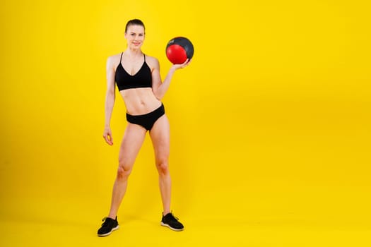 Portrait of a fitness happy fit woman standing holding a medicine ball. Copy Free space for text. Slim caucasian cross fit woman with fitness ball stand in gym, look. Plain light wall background