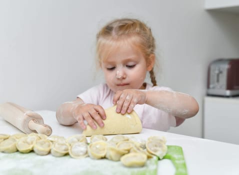Little girl in flour prepares dumplings in the kitchen