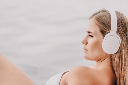 A woman wearing headphones is laying on a beach. She is wearing a white bikini top and is looking at the water