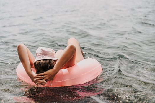 A woman is floating on a pink inflatable tube in the ocean. She is wearing a hat and has her hair down. The scene is peaceful and relaxing, with the woman enjoying her time in the water