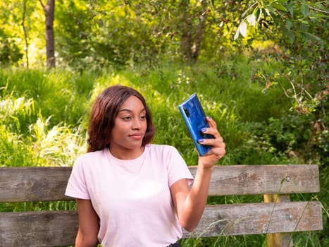 Young black woman with her phone taking selfie in a park on an October afternoon.