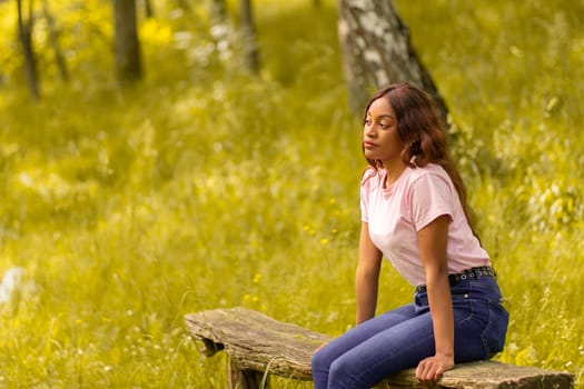 young black woman sitting on a bench in a park on a summer afternoon