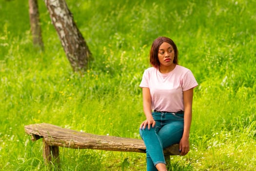 young black woman sitting on a bench in a park on a summer afternoon