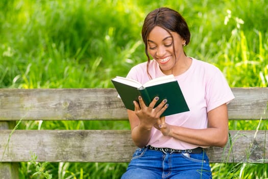 Young black woman sitting on a park bench reading a book.