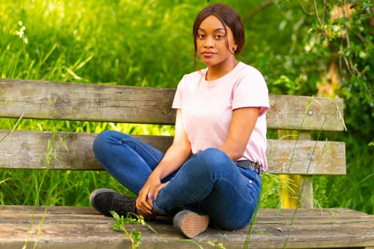 young black woman sitting on a bench in a park on a summer afternoon