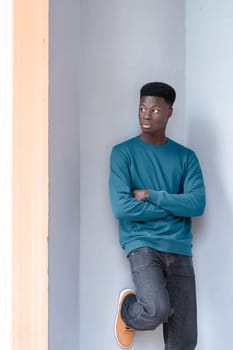 A man is leaning against a wall with his arms crossed in a confident posture.