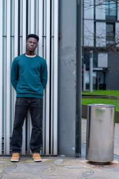 A young man in a green sweater stands in front of a trash can. The image has a casual and relaxed mood, as the man is simply posing for a photo