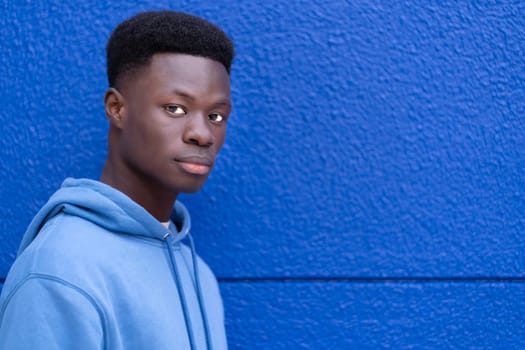 A man is standing in front of a blue wall, looking directly at the camera.