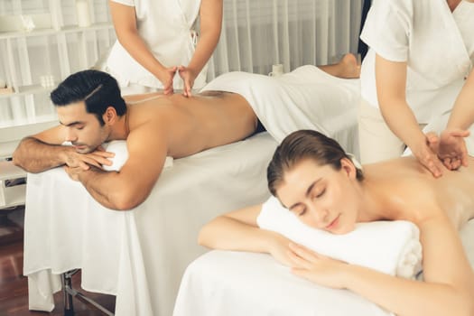 Caucasian couple customer enjoying relaxing anti-stress spa massage and pampering with beauty skin recreation leisure in day light ambient salon spa at luxury resort or hotel. Quiescent