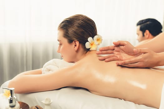 Caucasian couple customer enjoying relaxing anti-stress spa massage and pampering with beauty skin recreation leisure in day light ambient salon spa at luxury resort or hotel. Quiescent