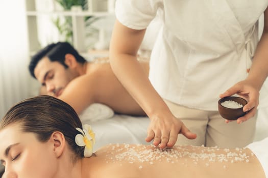 Blissful couple customer having exfoliation treatment in luxury spa salon with warmth candle light ambient. Salt scrub beauty treatment in health spa body scrub. Quiescent