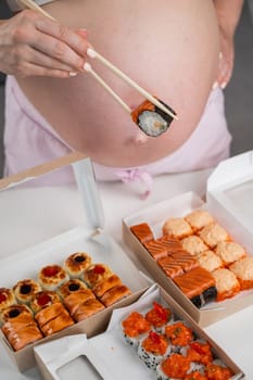 A pregnant woman stands at a table with rolls. Close-up of the belly