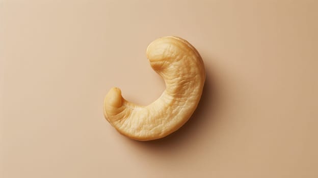 Single raw cashew nut on beige background, minimalistic food concept.