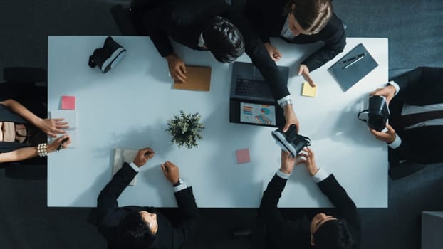 Top view of smart manager give vr head set to businesspeople while businesswoman prepare data analysis or analytic graph in laptop at meeting. Startup team preparing to enter meta verse. Directorate.