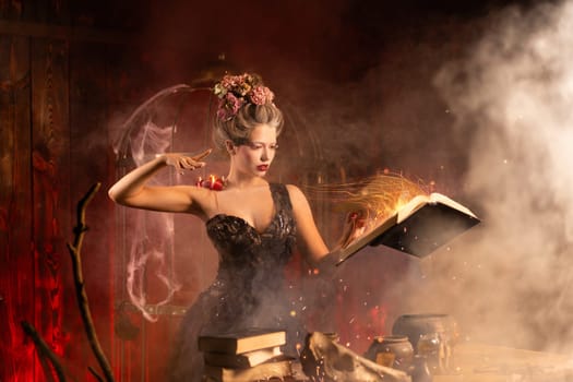 Attractive young woman dressed in vintage black gown, holding book of spells in old castle. Halloween celebration, witchcraft concept, fairy tale mystic atmosphere. Conjuring magic spells.