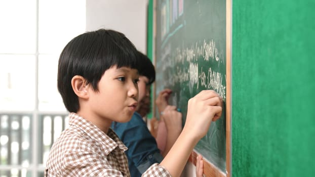 Side view of asian boy writing engineering prompt and programing system while standing blackboard with generated AI prompt written by attractive student at STEM technology lesson. Closeup. Pedagogy.