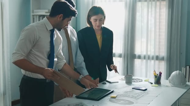 Professional engineer team in casual cloth talking about turbine engine structure at table with metal gear, calculator, sticky notes. Group of technician standing and attend in meeting. Alimentation.