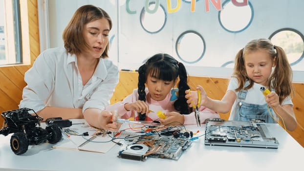 Skilled caucasian teacher teach and explain students about digital electrical tool. Expert girl learn electronic equipment and use to fix motherboard at table with chips and wires placed. Erudition.