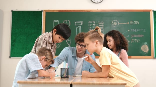 Smart teacher explain idea while diverse children drawing mind map while group of diverse student working together to do class work. Attractive instructor teaching and talking about working. Pedagogy.